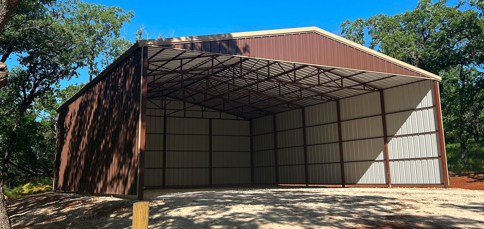 Metal building with open front, brown and white exterior, in a wooded area.