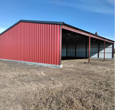 Red metal barn with open side in a field.